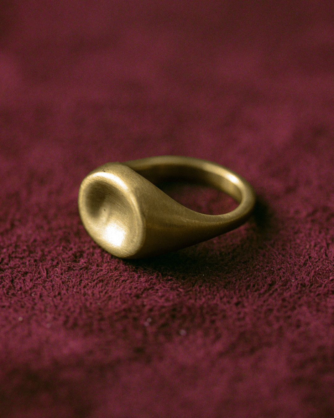 Gold concave signet ring by dear_ jewelry photographed on burgundy fabric.